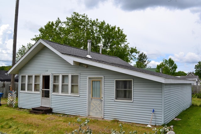 back of property featuring a yard, fence, and roof with shingles