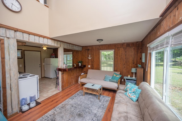 living room featuring light wood finished floors, wood walls, and a towering ceiling