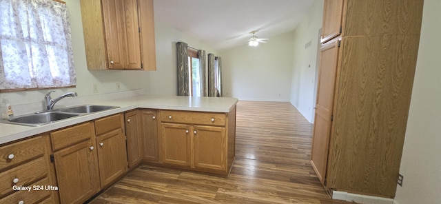 kitchen featuring wood finished floors, brown cabinetry, a peninsula, a sink, and light countertops