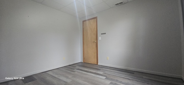 spare room featuring wood finished floors, visible vents, a drop ceiling, and baseboards