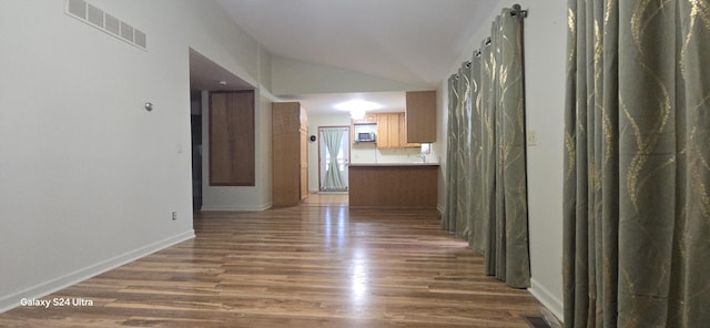 corridor with lofted ceiling, wood finished floors, visible vents, and baseboards