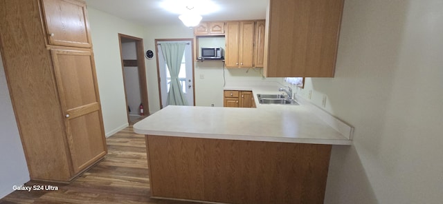 kitchen featuring stainless steel microwave, light countertops, a peninsula, wood finished floors, and a sink