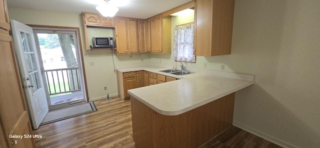 kitchen featuring dark wood finished floors, stainless steel microwave, a peninsula, and a sink