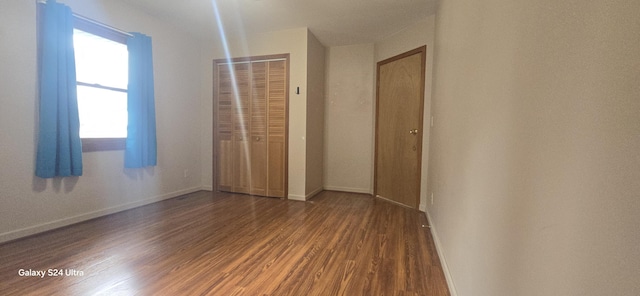 unfurnished bedroom featuring wood finished floors, baseboards, and a closet