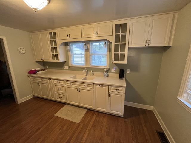 kitchen featuring dark wood-style floors, baseboards, a sink, light countertops, and white cabinetry