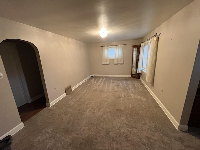 carpeted empty room featuring baseboards and arched walkways