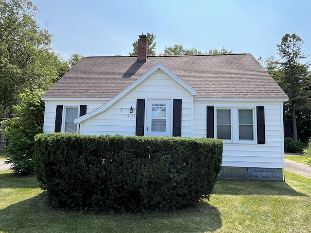 bungalow-style home with a chimney, a front yard, and a shingled roof