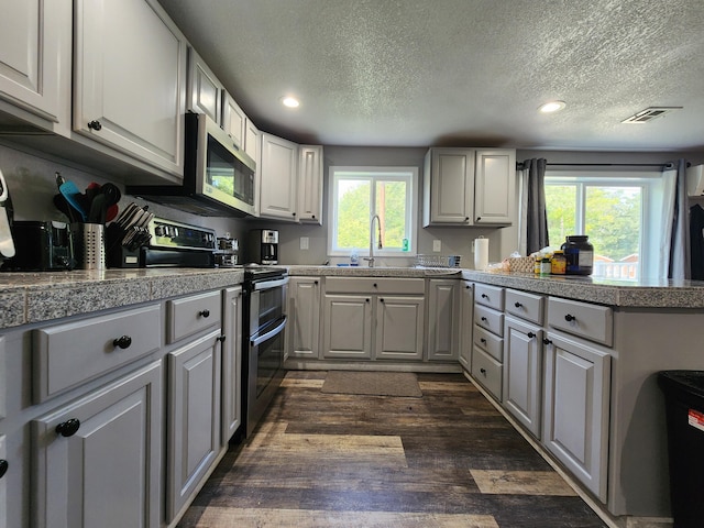 kitchen featuring visible vents, dark wood-style flooring, a sink, stainless steel appliances, and tile counters