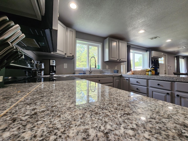 kitchen featuring visible vents, tile counters, an AC wall unit, a textured ceiling, and a sink