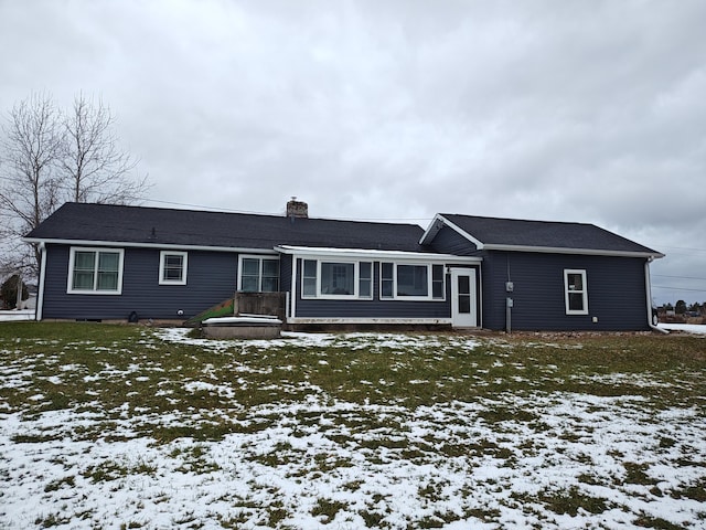 snow covered rear of property with a chimney