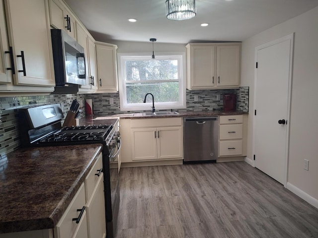 kitchen featuring light wood-type flooring, a sink, dark countertops, stainless steel appliances, and hanging light fixtures