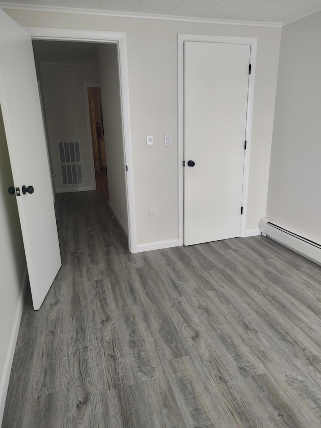 unfurnished bedroom with visible vents, ornamental molding, wood finished floors, a baseboard radiator, and baseboards