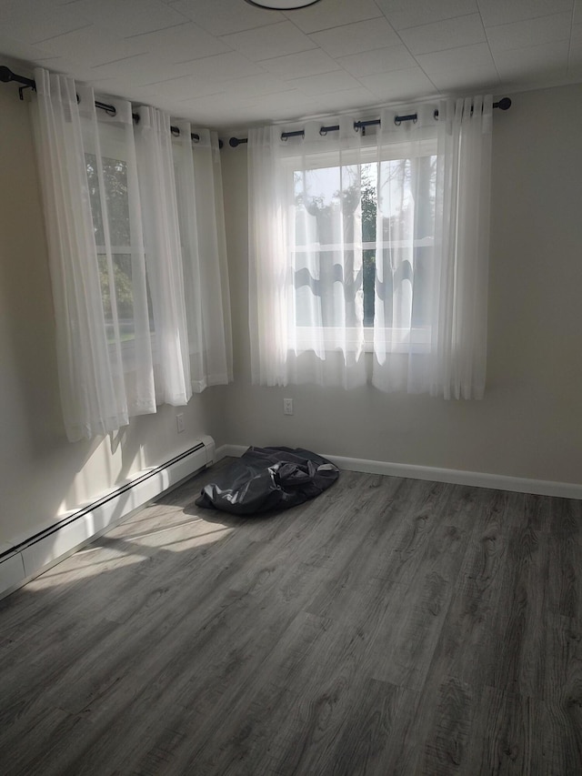 empty room featuring wood finished floors, baseboards, and a baseboard radiator