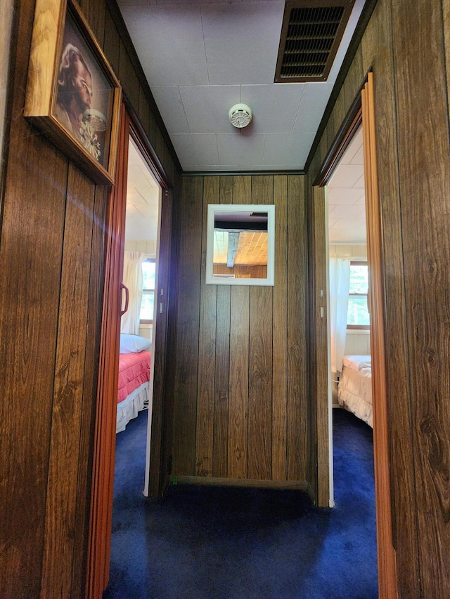 hallway featuring carpet flooring, visible vents, wood walls, and plenty of natural light