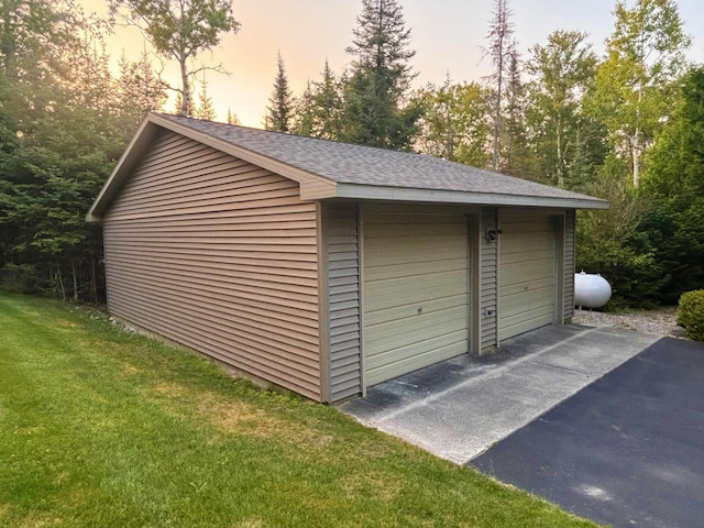 garage at dusk featuring a garage and a lawn