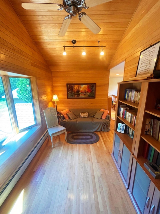 living area with light wood finished floors, baseboard heating, wooden walls, and vaulted ceiling