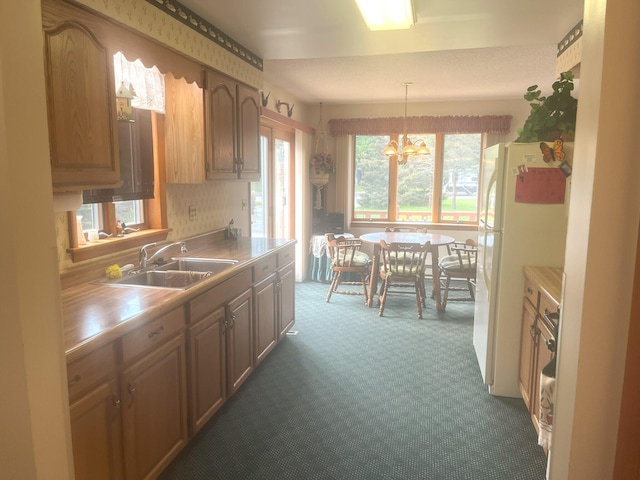 kitchen with a notable chandelier, a sink, dark carpet, freestanding refrigerator, and light countertops