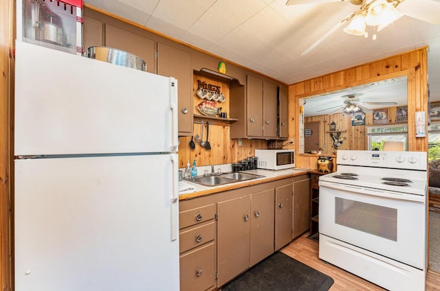 kitchen featuring white appliances, a ceiling fan, a sink, wooden walls, and light wood-style flooring