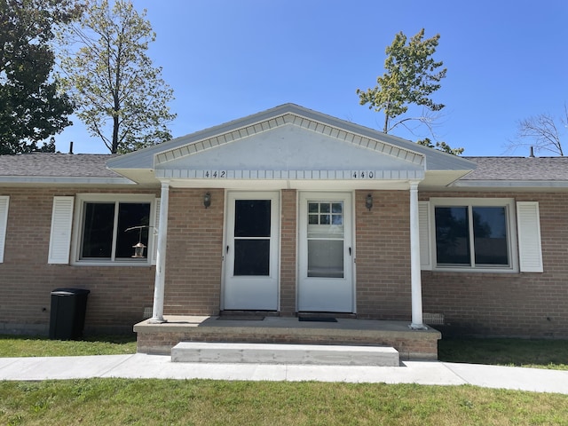 view of front of house featuring brick siding and roof with shingles