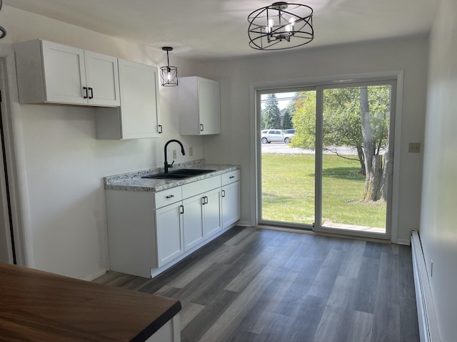 kitchen with wood finished floors, white cabinetry, a sink, hanging light fixtures, and a baseboard heating unit