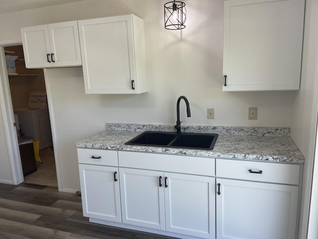 kitchen featuring light stone countertops, washer / dryer, dark wood-style flooring, a sink, and white cabinets