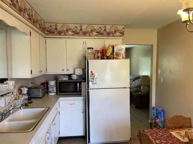 kitchen featuring a sink, stainless steel microwave, white cabinets, and freestanding refrigerator