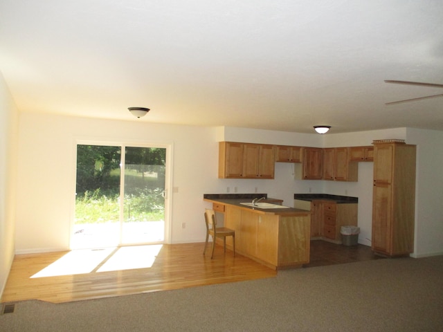 kitchen featuring visible vents, brown cabinets, a peninsula, dark countertops, and light wood-type flooring