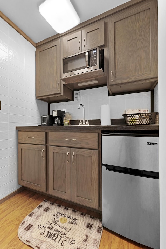 kitchen featuring stainless steel microwave, dark countertops, light wood-style floors, and dishwashing machine