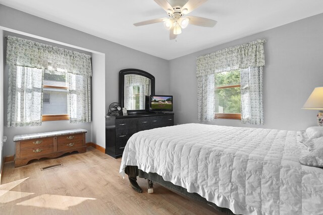 bedroom with ceiling fan, light wood-style floors, visible vents, and baseboards