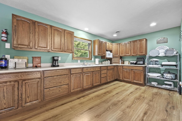 kitchen with light countertops, brown cabinetry, light wood-style floors, and white microwave