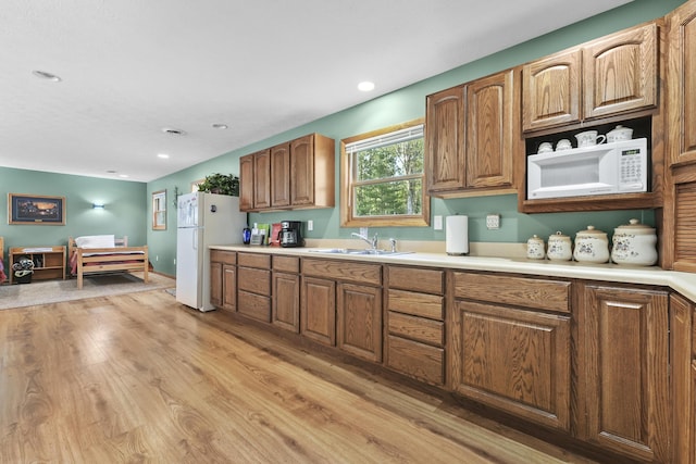 kitchen featuring white appliances, recessed lighting, a sink, light countertops, and light wood-type flooring