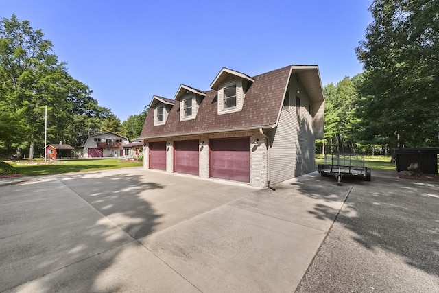 view of side of property featuring a gambrel roof, brick siding, roof with shingles, and concrete driveway