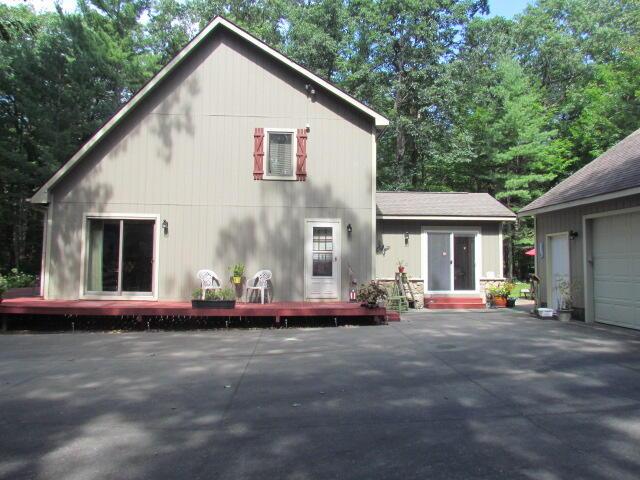 rear view of house featuring driveway, a wooden deck, a garage, and a patio