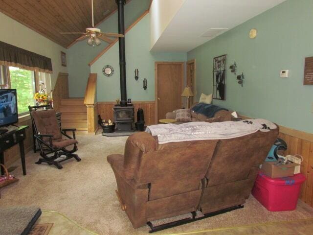 carpeted living area featuring vaulted ceiling, a wood stove, wood walls, and wainscoting