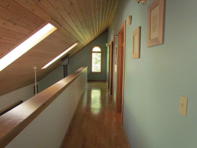 corridor featuring lofted ceiling with skylight, wood ceiling, an upstairs landing, and wood finished floors