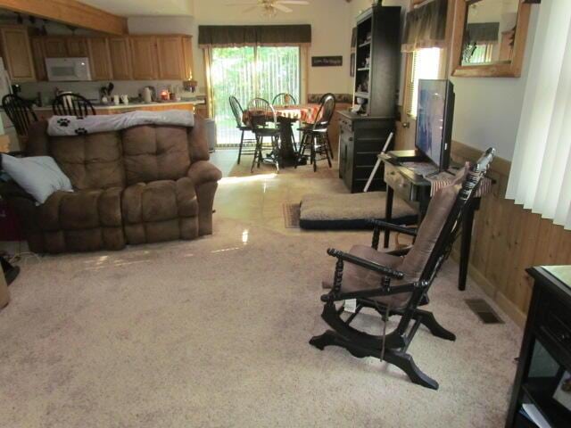 living room with light carpet, visible vents, wood walls, and ceiling fan