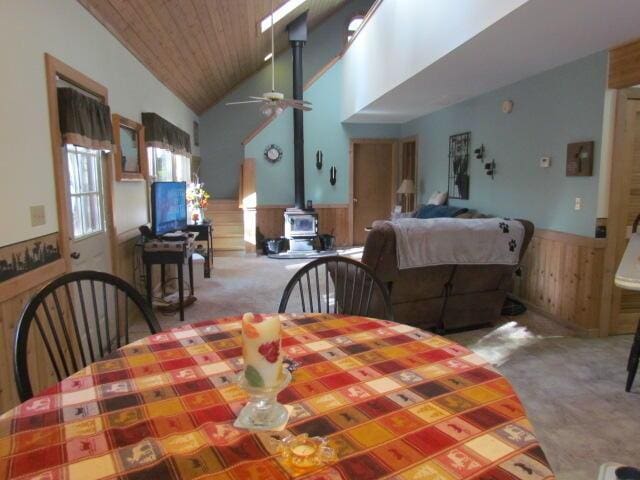 carpeted dining area with a ceiling fan, a wainscoted wall, a wood stove, wood ceiling, and wood walls