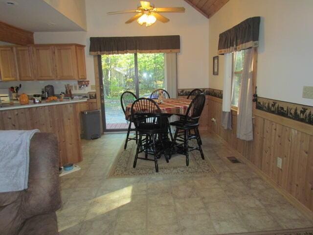 dining area with wooden walls, visible vents, ceiling fan, wainscoting, and high vaulted ceiling