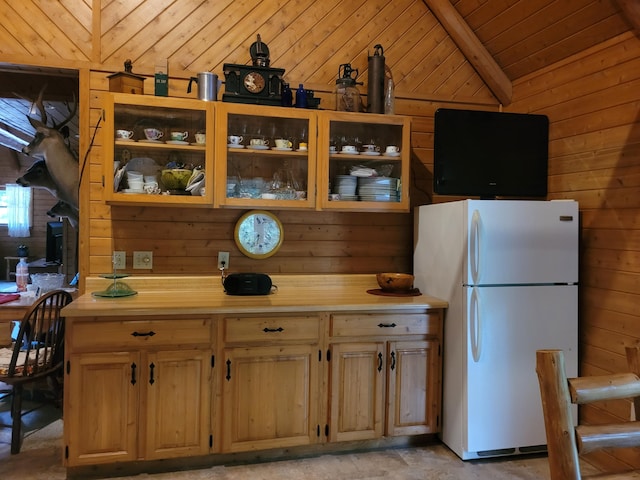 kitchen with light countertops, wood walls, freestanding refrigerator, and vaulted ceiling