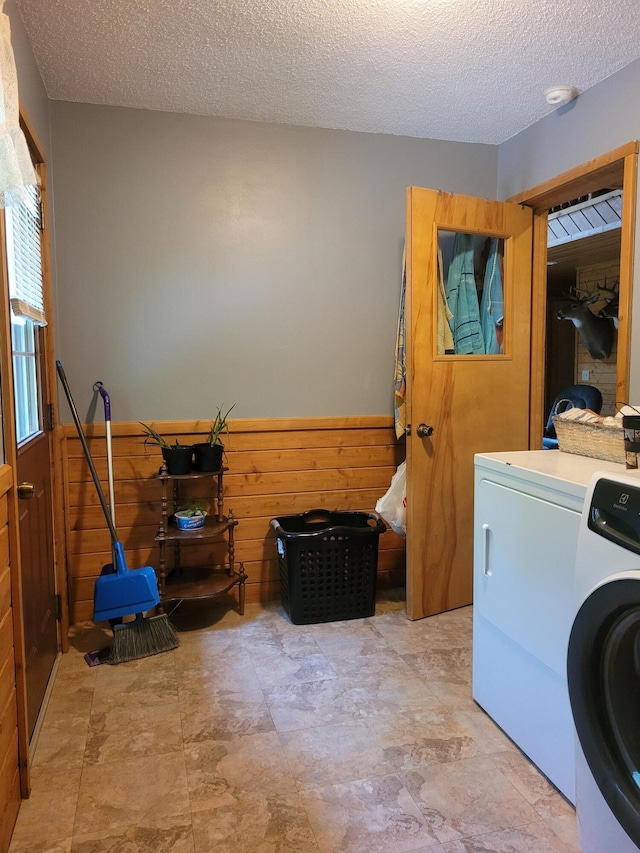 laundry room featuring laundry area, wainscoting, wood walls, a textured ceiling, and washer and clothes dryer