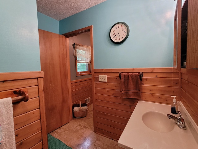 bathroom featuring a wainscoted wall, visible vents, a textured ceiling, wooden walls, and vanity