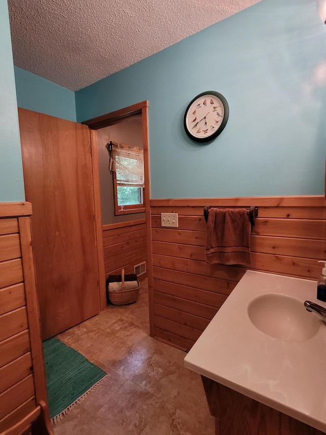 bathroom featuring a wainscoted wall, visible vents, a textured ceiling, wooden walls, and vanity