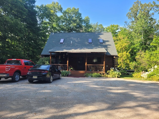 view of front of house featuring log siding, a porch, a shingled roof, and gravel driveway