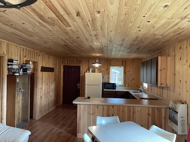 kitchen with dark wood-type flooring, black microwave, a peninsula, freestanding refrigerator, and heating unit