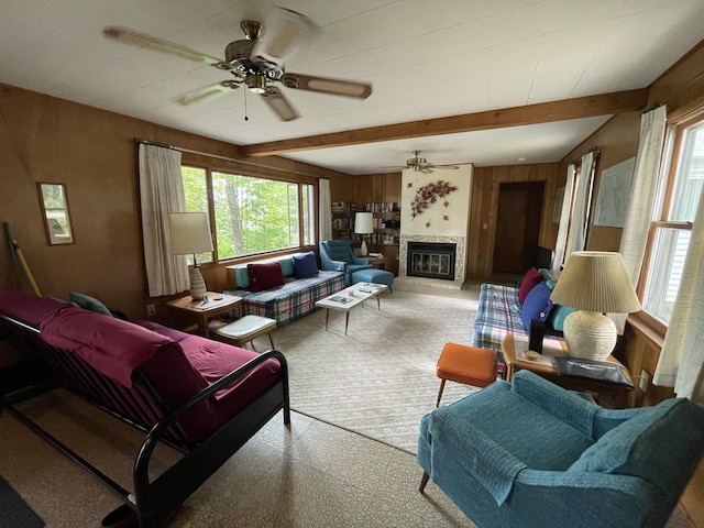 living room with a glass covered fireplace, beam ceiling, wooden walls, and a ceiling fan