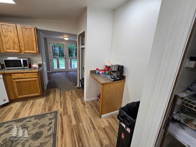 kitchen with brown cabinets, lofted ceiling, stainless steel microwave, light wood finished floors, and baseboards