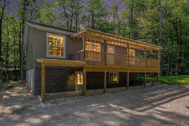 rear view of property featuring stone siding, a wooden deck, gravel driveway, and a forest view