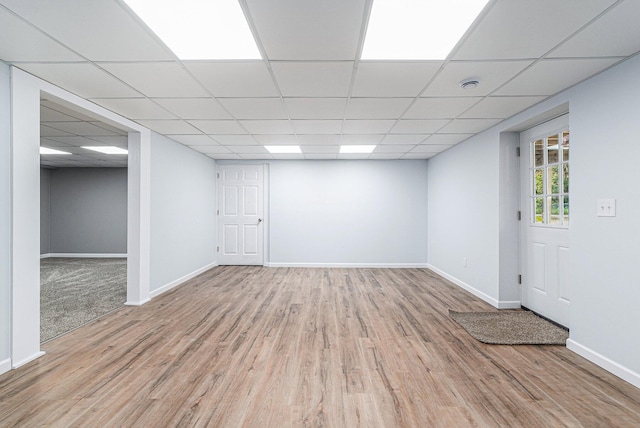interior space featuring a paneled ceiling, baseboards, and light wood finished floors