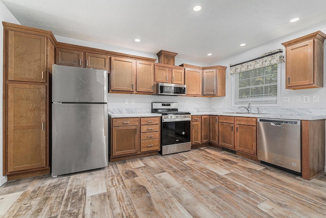 kitchen featuring light wood-style flooring, a sink, appliances with stainless steel finishes, brown cabinetry, and light countertops