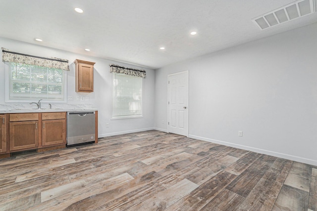 kitchen with visible vents, light wood-type flooring, stainless steel dishwasher, brown cabinetry, and a sink